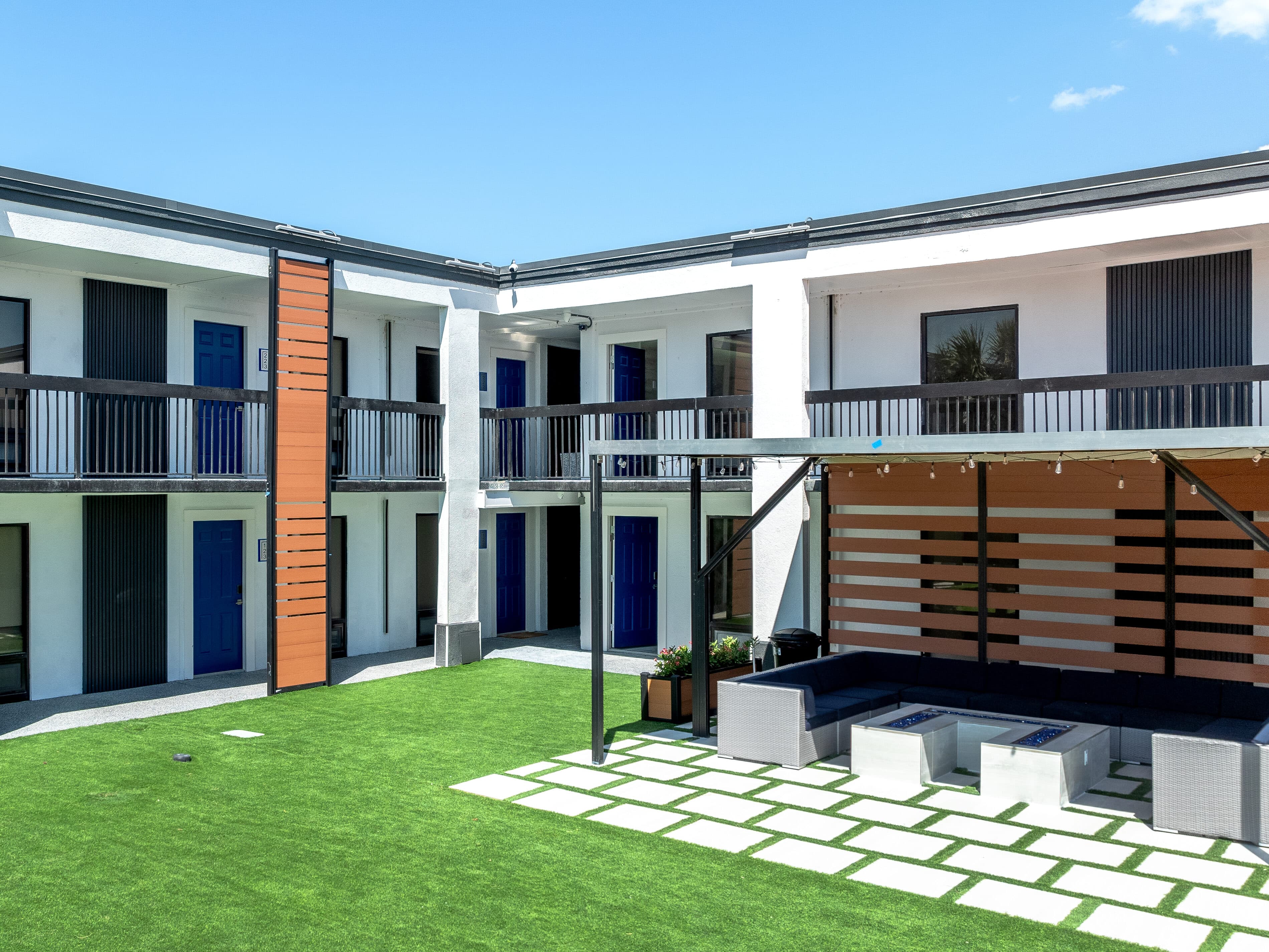 The same building corner after conversion: white facade, blue doors, wood-slat panels and the turf courtyard lounge