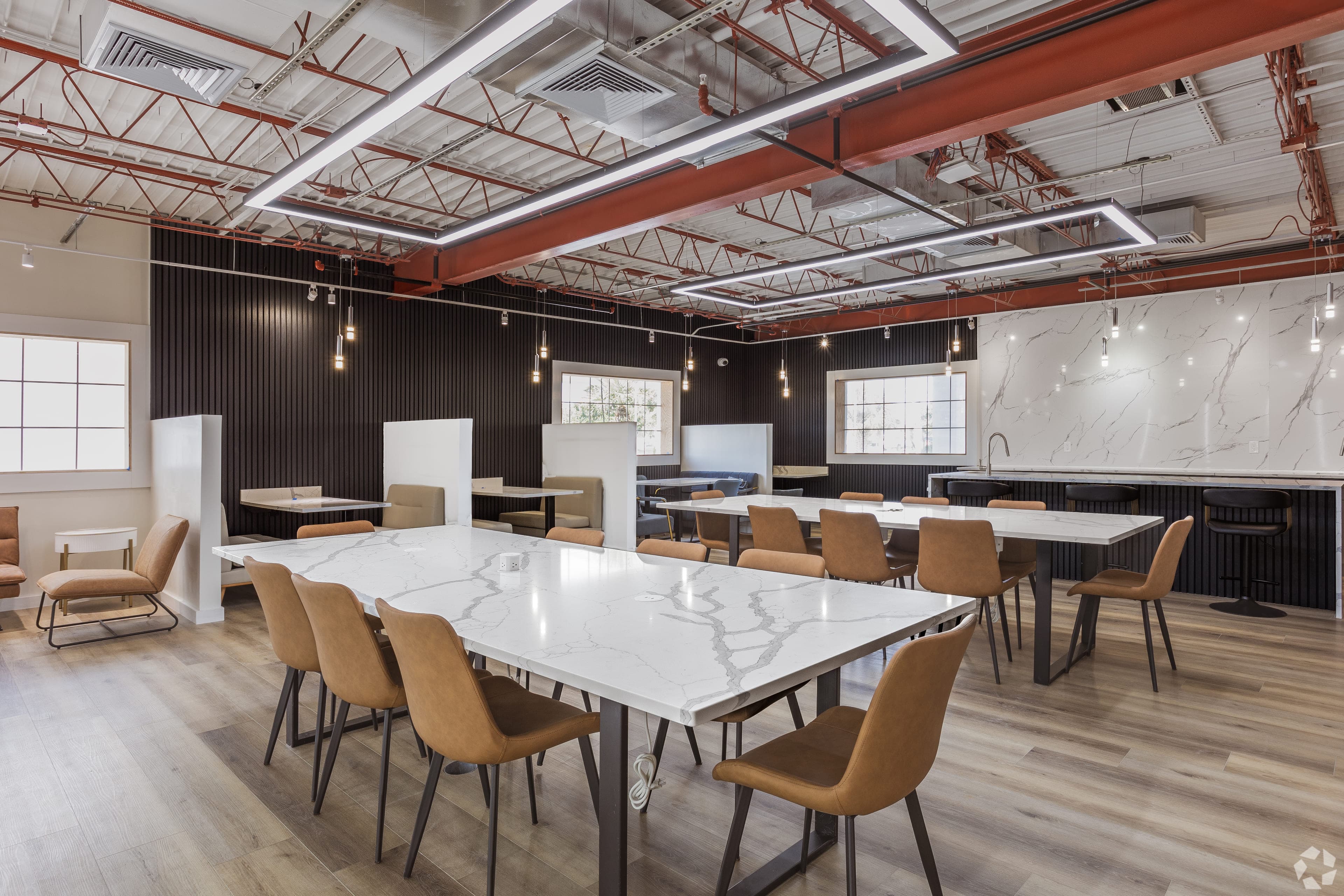 The resident coworking lounge at The Jade Winter Haven: exposed trusses, pendant lighting, and marble work tables in the converted community