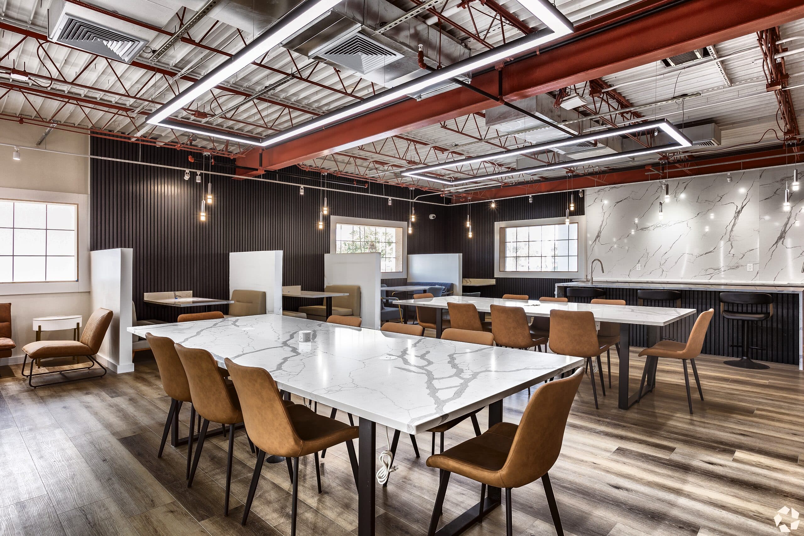 The resident coworking lounge at The Jade Winter Haven: exposed trusses, pendant lighting, and marble work tables in the converted community