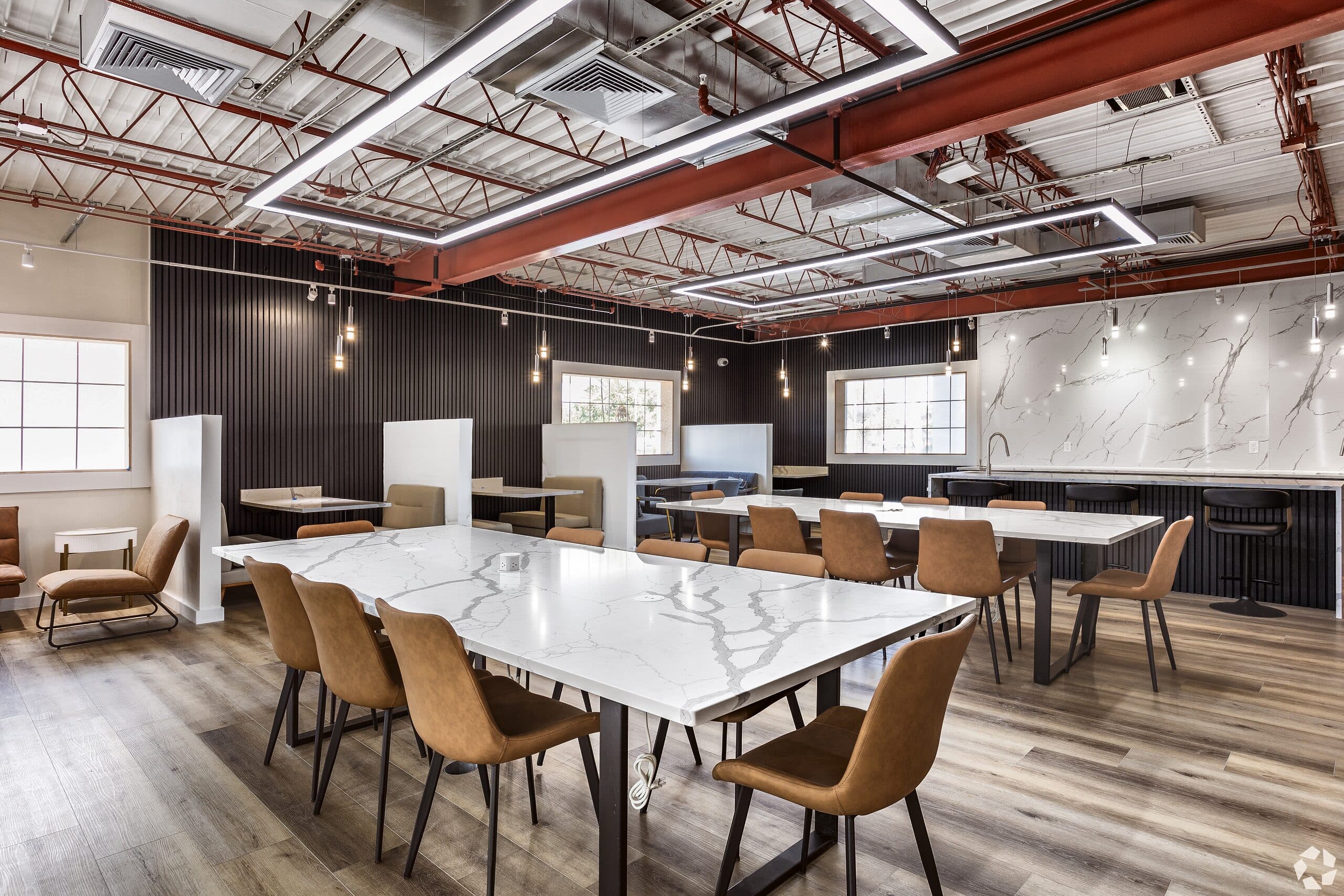 The resident coworking lounge at The Jade Winter Haven: exposed trusses, pendant lighting, and marble work tables in the converted community